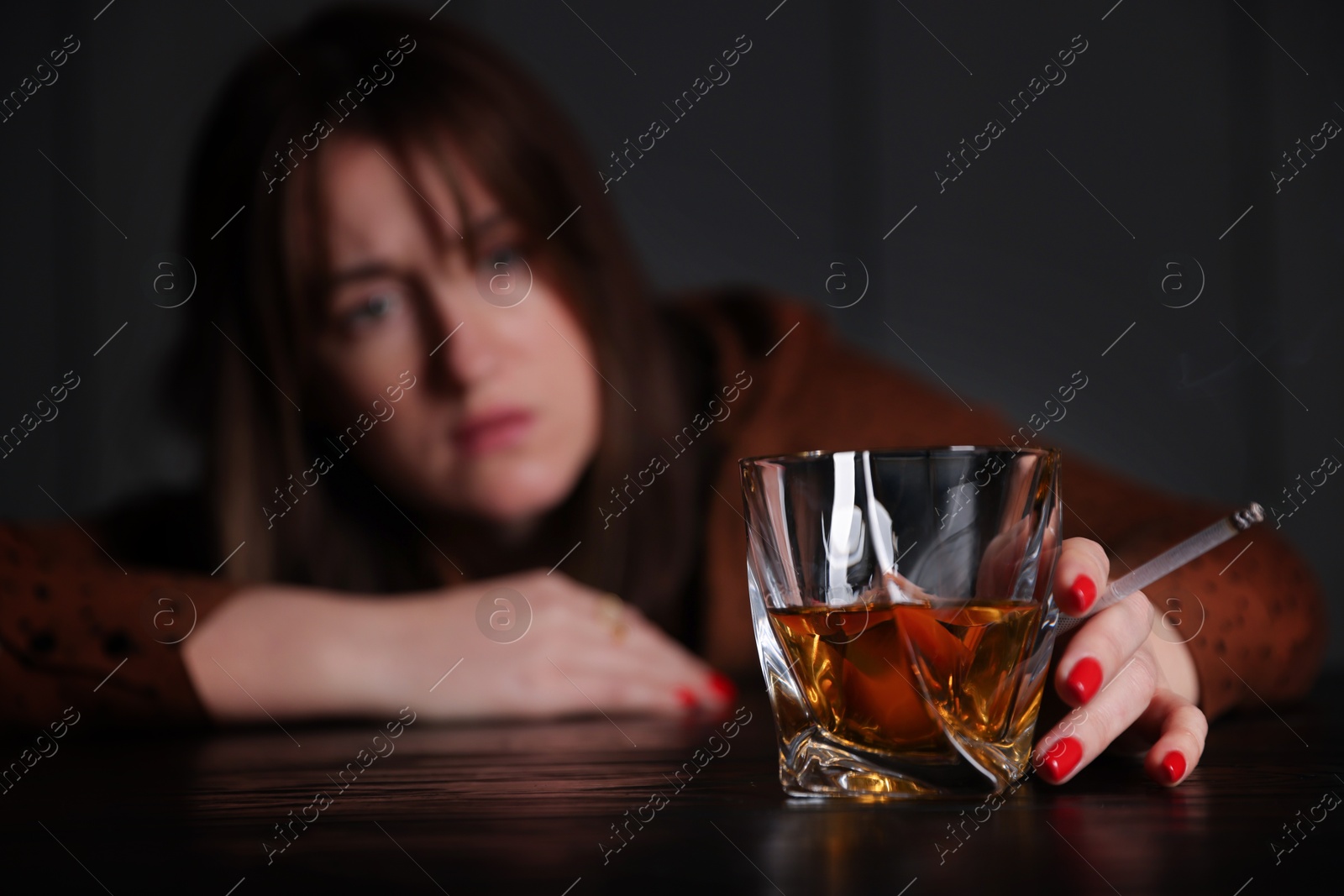 Photo of Alcohol addiction. Woman with glass of whiskey and cigarette at table indoors, selective focus