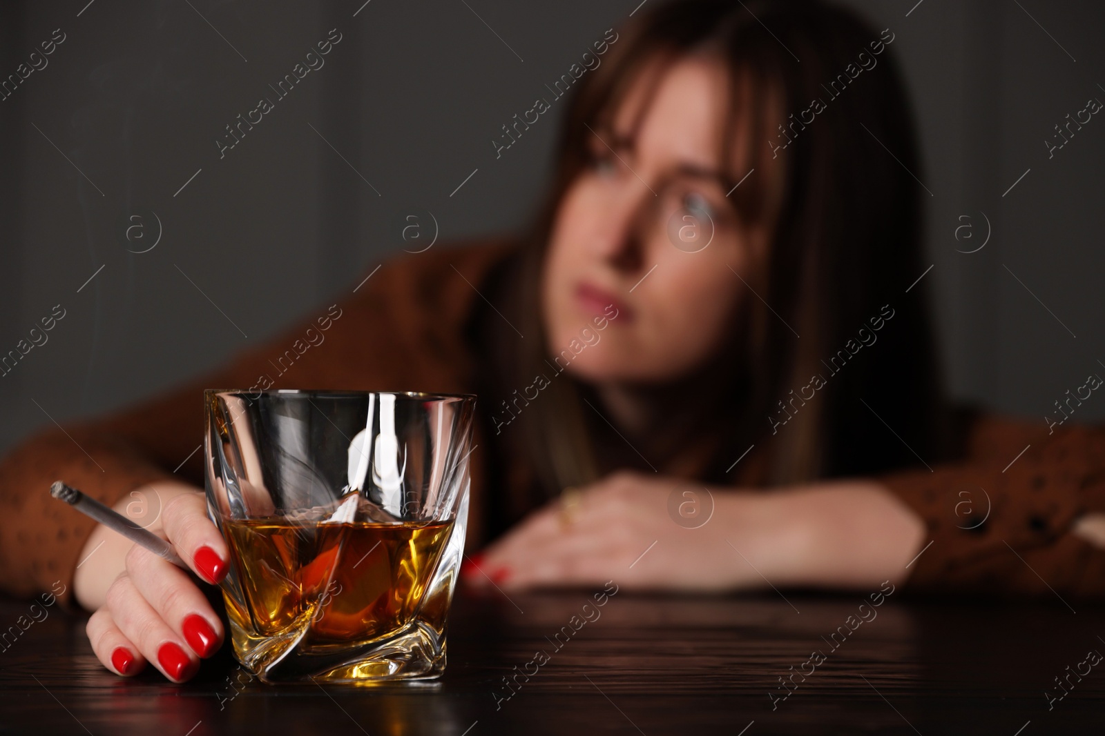 Photo of Alcohol addiction. Woman with glass of whiskey and cigarette at table indoors, selective focus