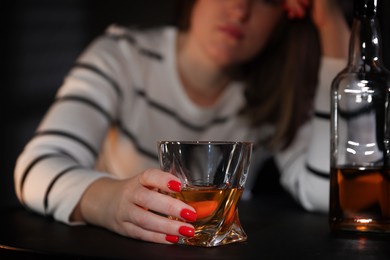 Photo of Alcohol addiction. Woman with glass of whiskey and bottle at table indoors, closeup