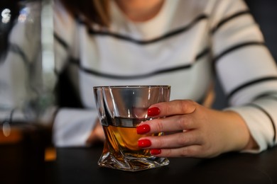 Photo of Alcohol addiction. Woman with glass of whiskey at table indoors, closeup