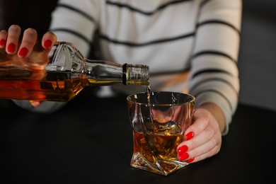 Photo of Alcohol addiction. Woman pouring whiskey from bottle into glass indoors, closeup