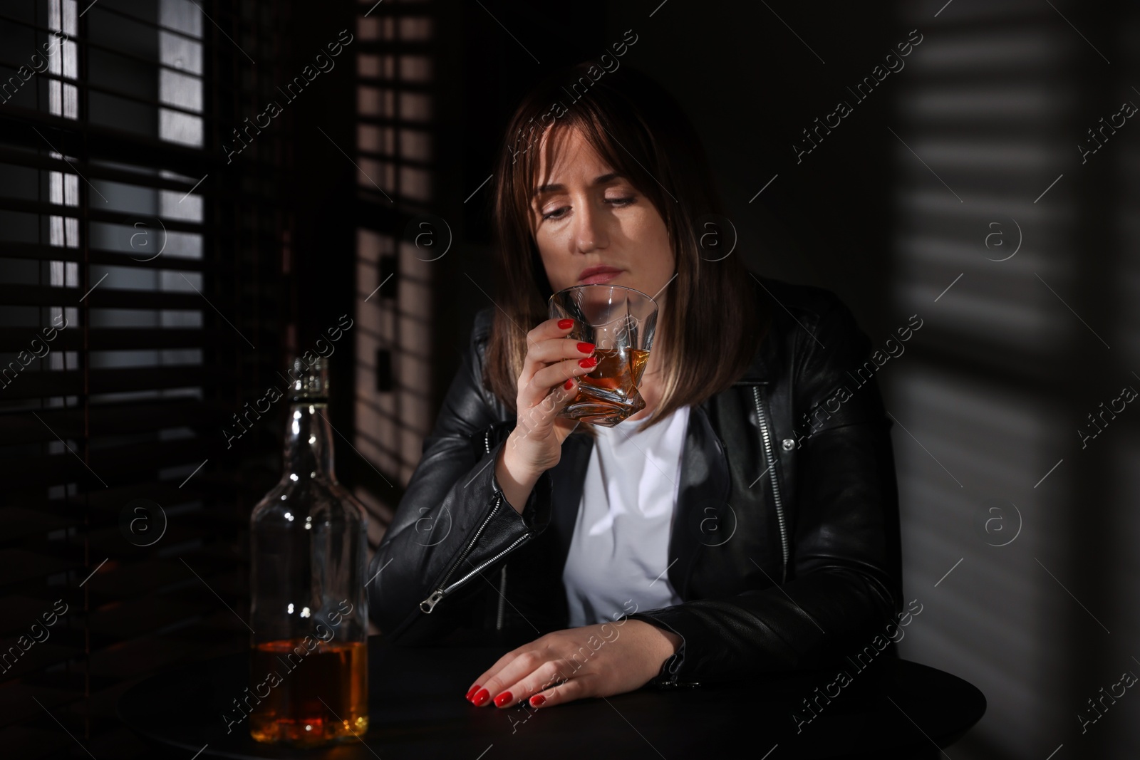 Photo of Alcohol addiction. Woman with glass of whiskey and bottle at table indoors