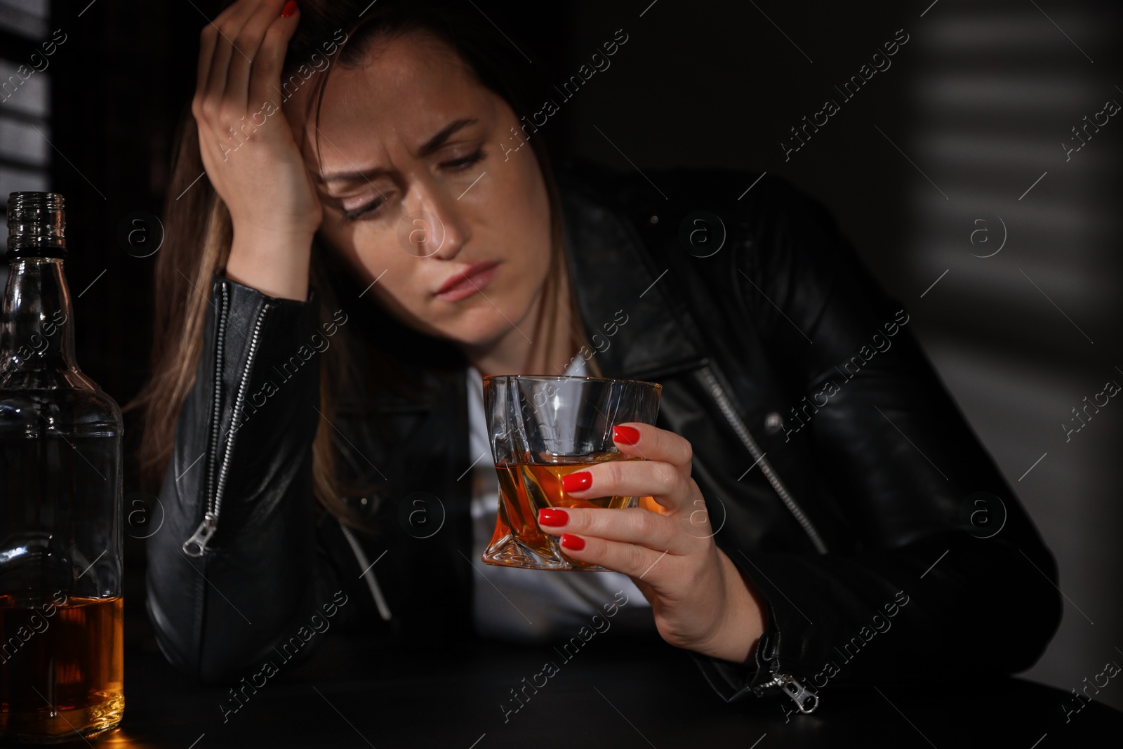 Photo of Alcohol addiction. Woman with glass of whiskey and bottle at table indoors