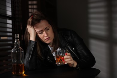 Photo of Alcohol addiction. Woman with glass of whiskey and bottle at table indoors