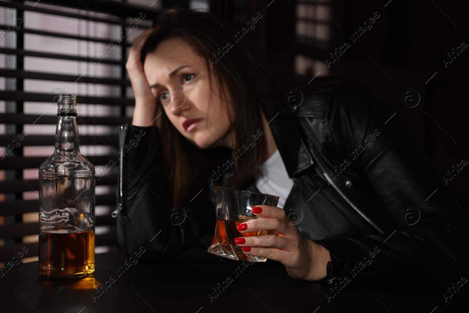 Photo of Alcohol addiction. Woman with glass of whiskey and bottle at table indoors