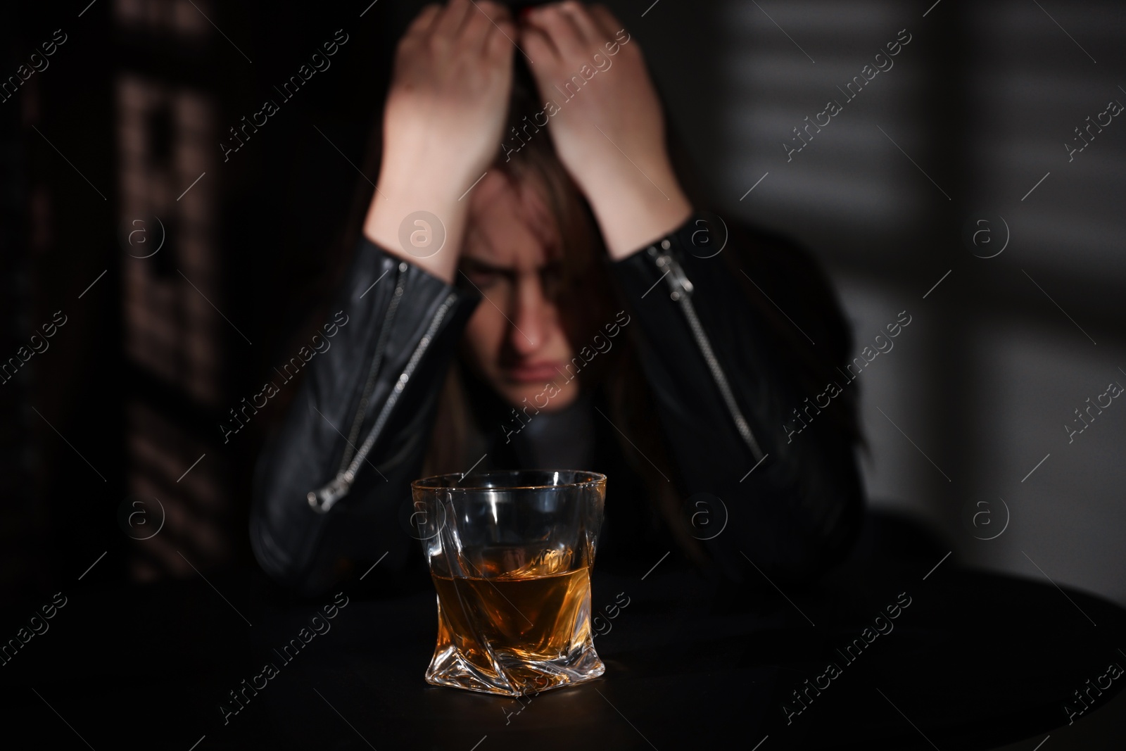 Photo of Alcohol addiction. Woman at table indoors, focus on glass of whiskey