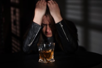 Photo of Alcohol addiction. Woman at table indoors, focus on glass of whiskey