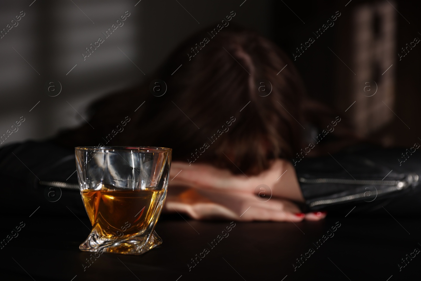 Photo of Alcohol addiction. Woman at table indoors, focus on glass of whiskey