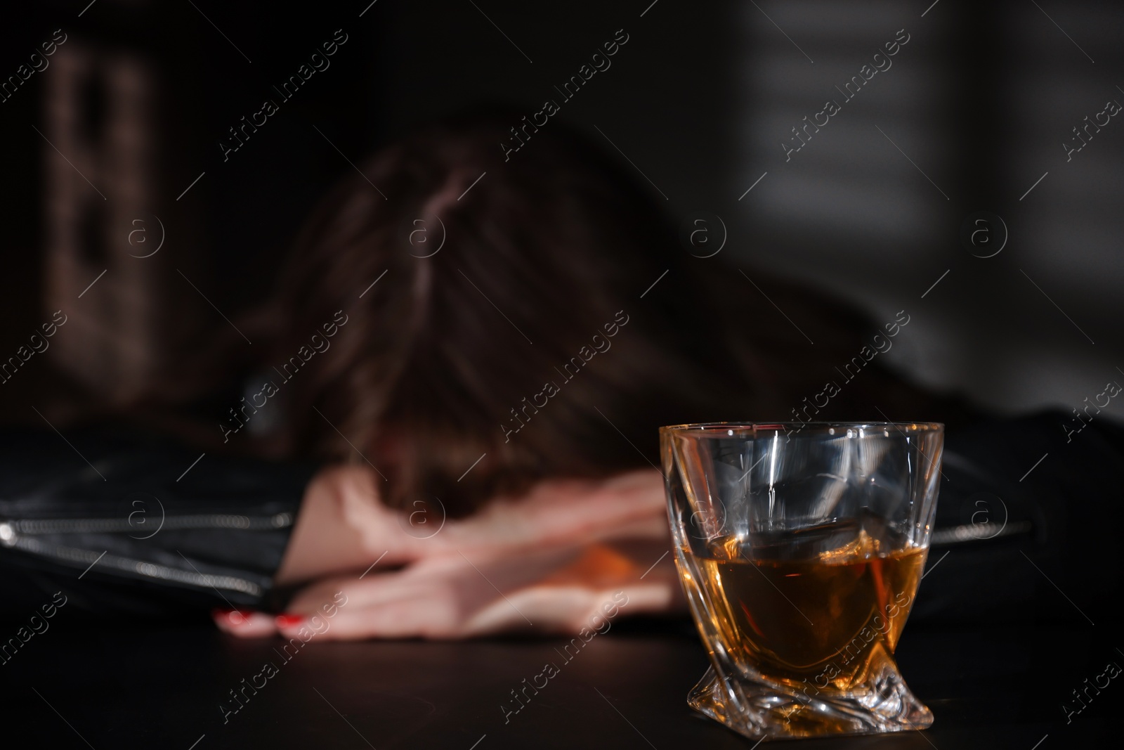 Photo of Alcohol addiction. Woman at table indoors, focus on glass of whiskey