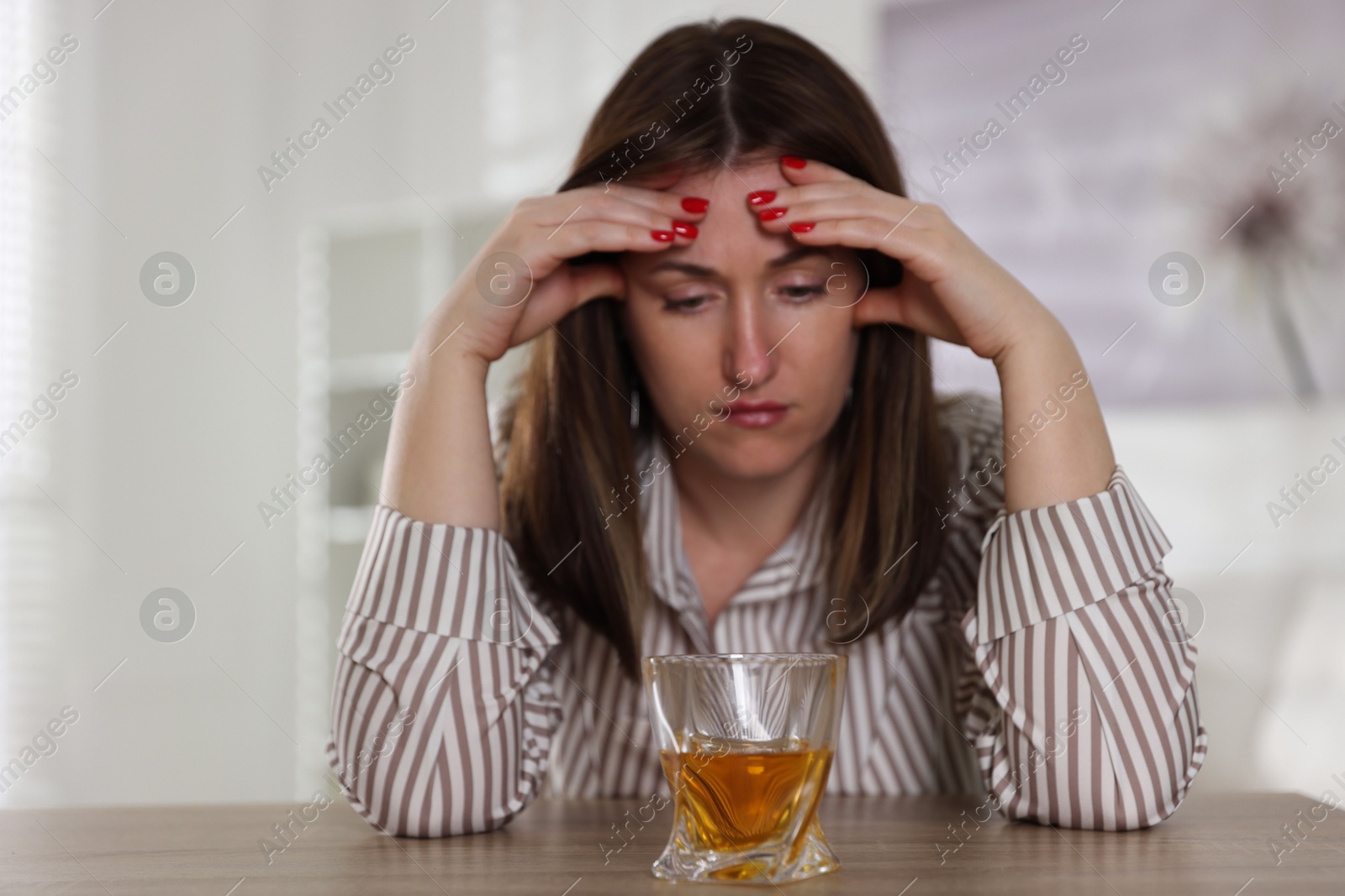 Photo of Alcohol addiction. Woman at wooden table with glass of whiskey indoors, selective focus