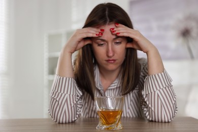 Photo of Alcohol addiction. Woman at wooden table with glass of whiskey indoors, selective focus