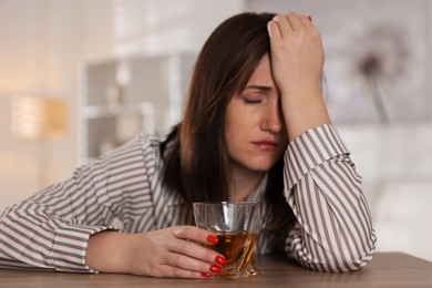 Photo of Alcohol addiction. Woman with glass of whiskey at wooden table indoors