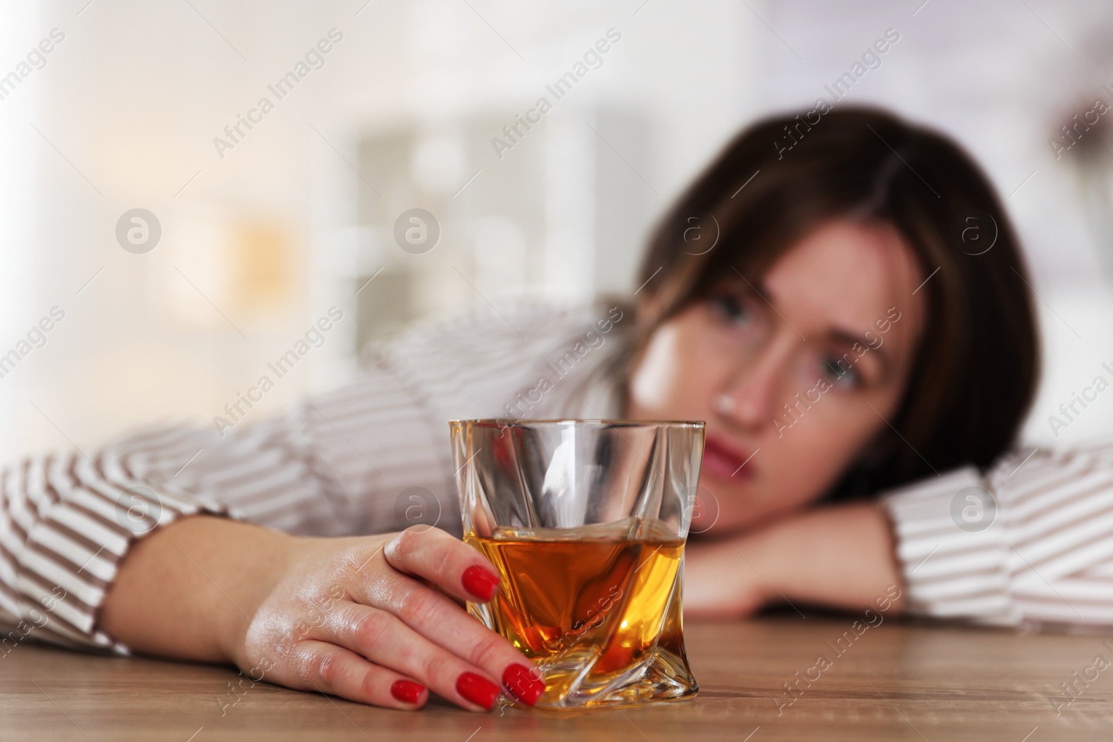 Photo of Alcohol addiction. Woman with glass of whiskey at wooden table indoors, selective focus