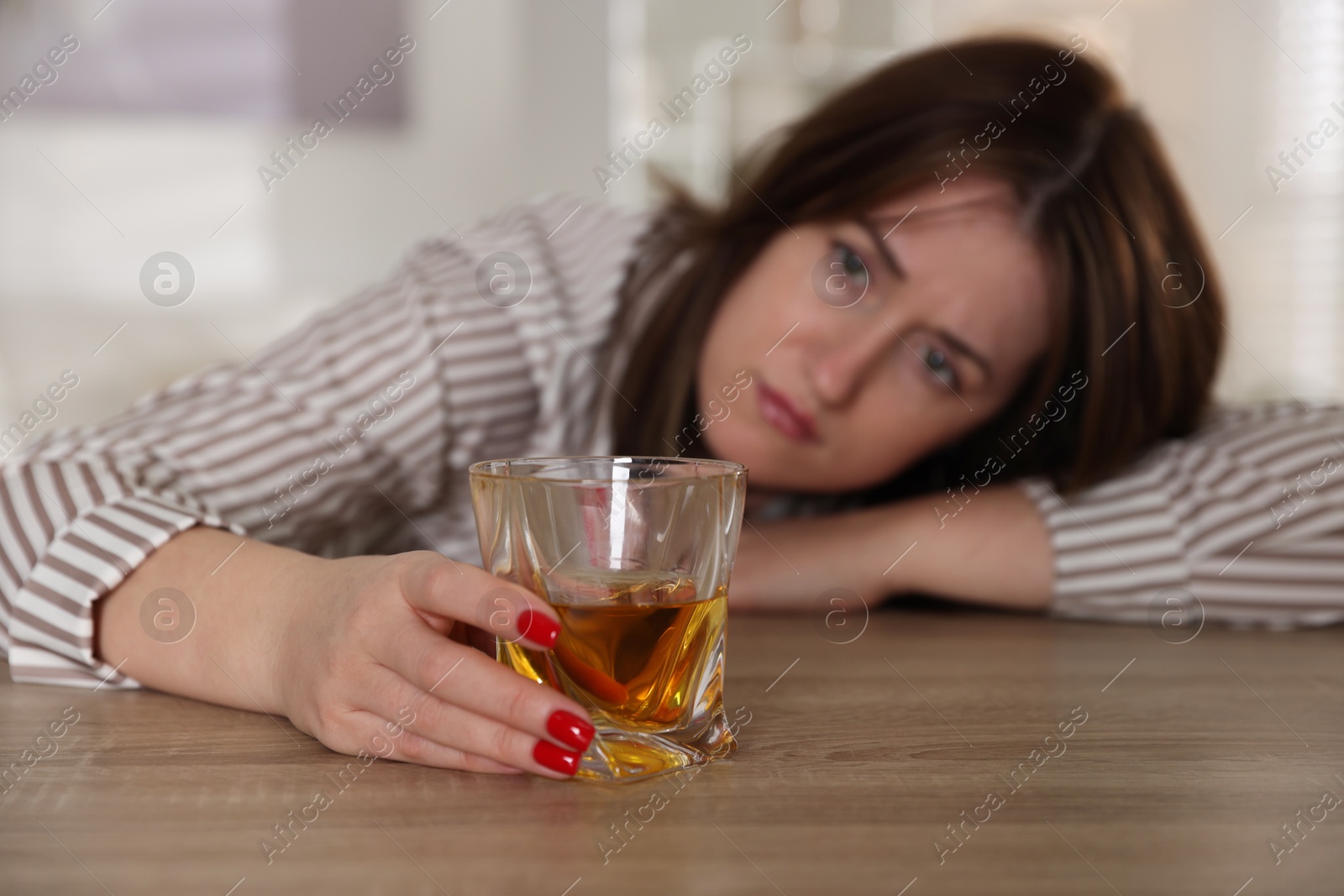 Photo of Alcohol addiction. Woman with glass of whiskey at wooden table indoors, selective focus