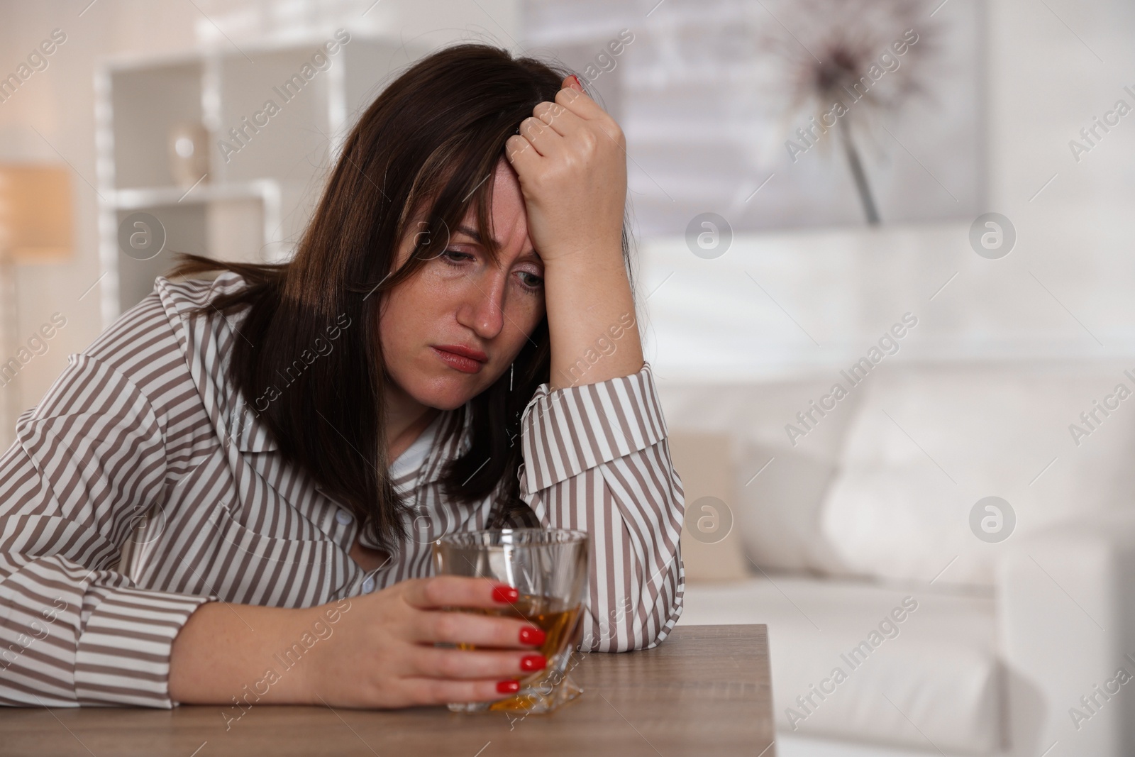 Photo of Alcohol addiction. Woman with glass of whiskey at wooden table indoors, space for text