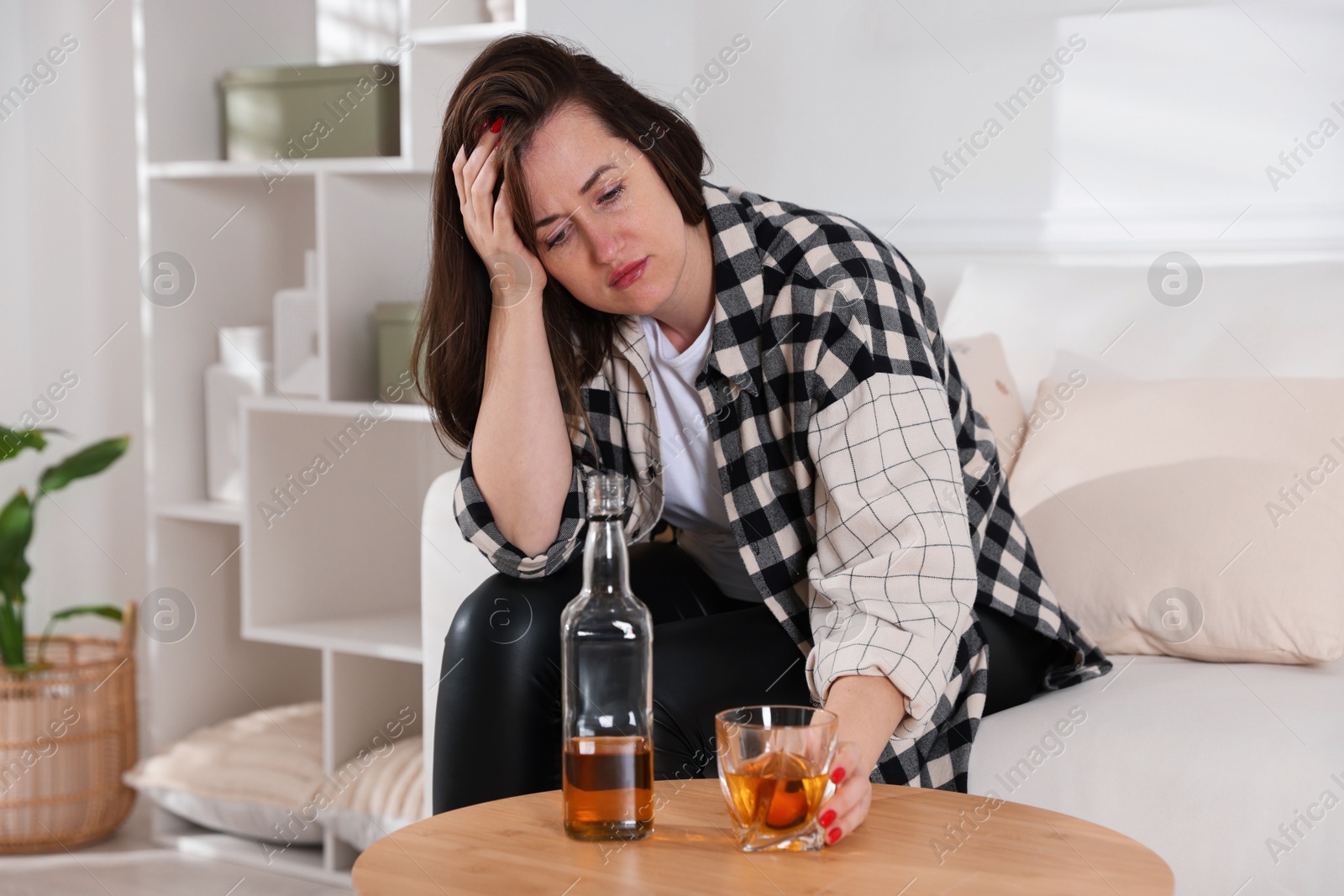 Photo of Alcohol addiction. Woman with glass of whiskey and bottle at home