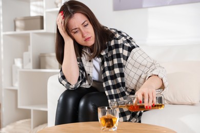 Photo of Alcohol addiction. Woman pouring whiskey into glass at table indoors