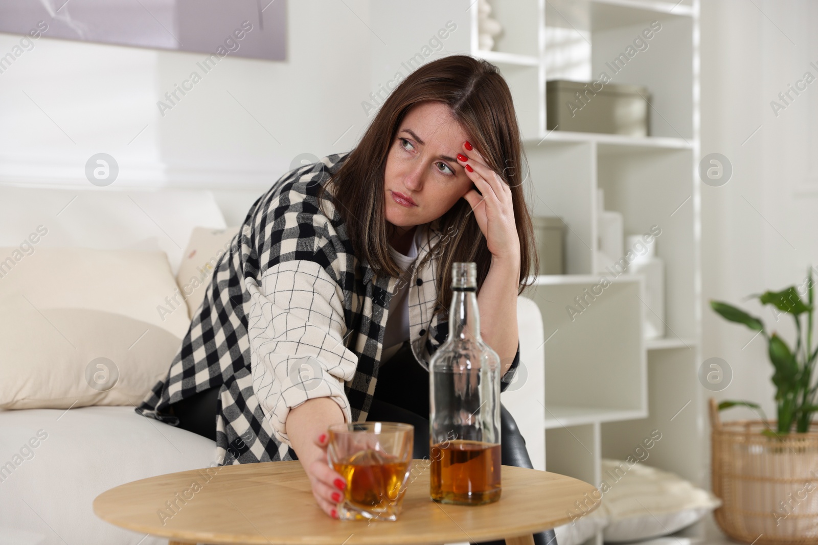 Photo of Alcohol addiction. Woman with glass of whiskey and bottle at home