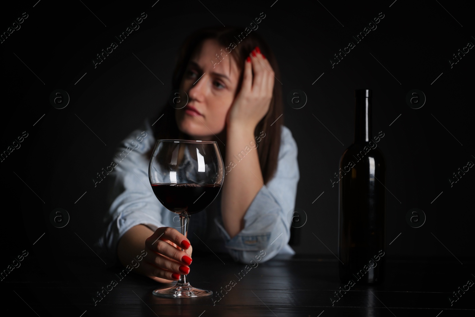 Photo of Alcohol addiction. Miserable woman with wine at table in dark, selective focus