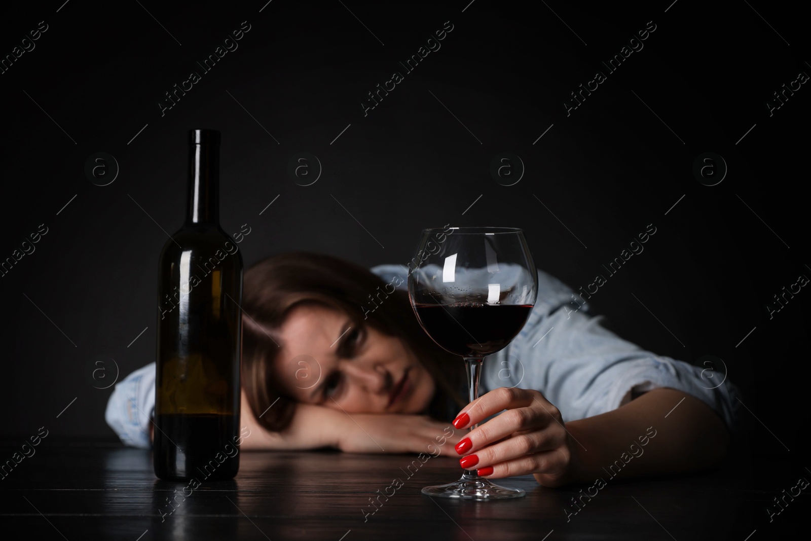 Photo of Alcohol addiction. Miserable woman with wine at table in dark, selective focus