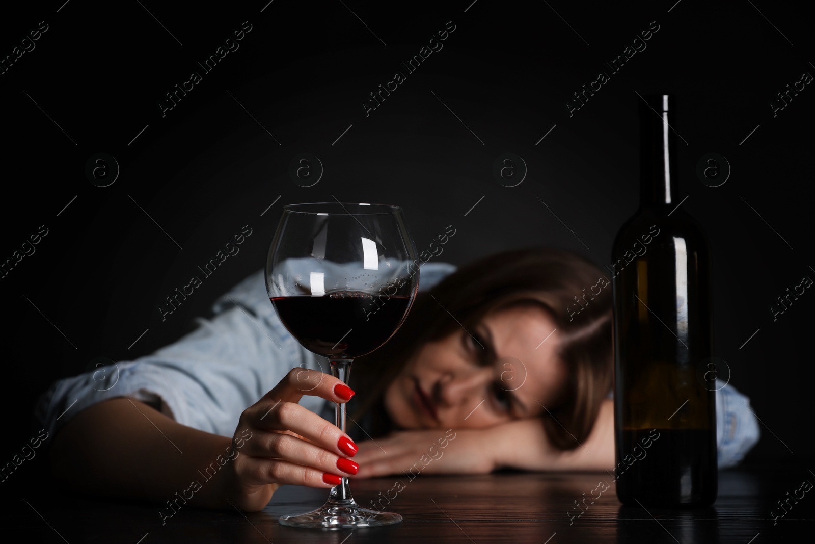 Photo of Alcohol addiction. Miserable woman with wine at table in dark, selective focus