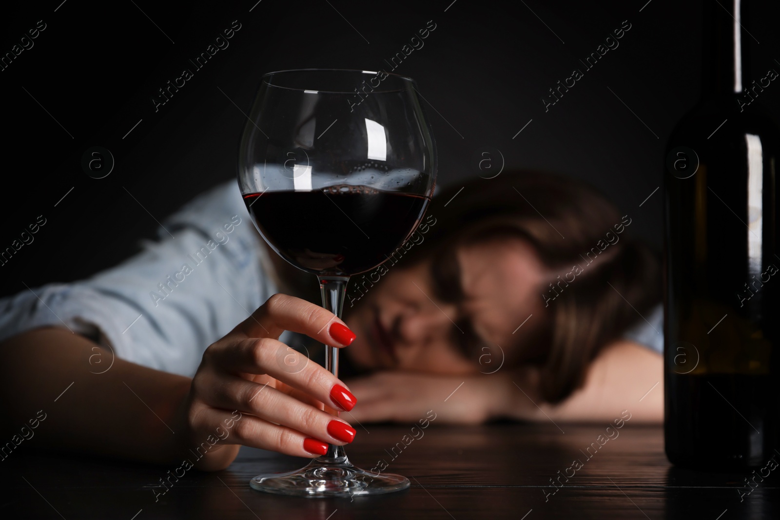 Photo of Alcohol addiction. Miserable woman with wine at table in dark, selective focus