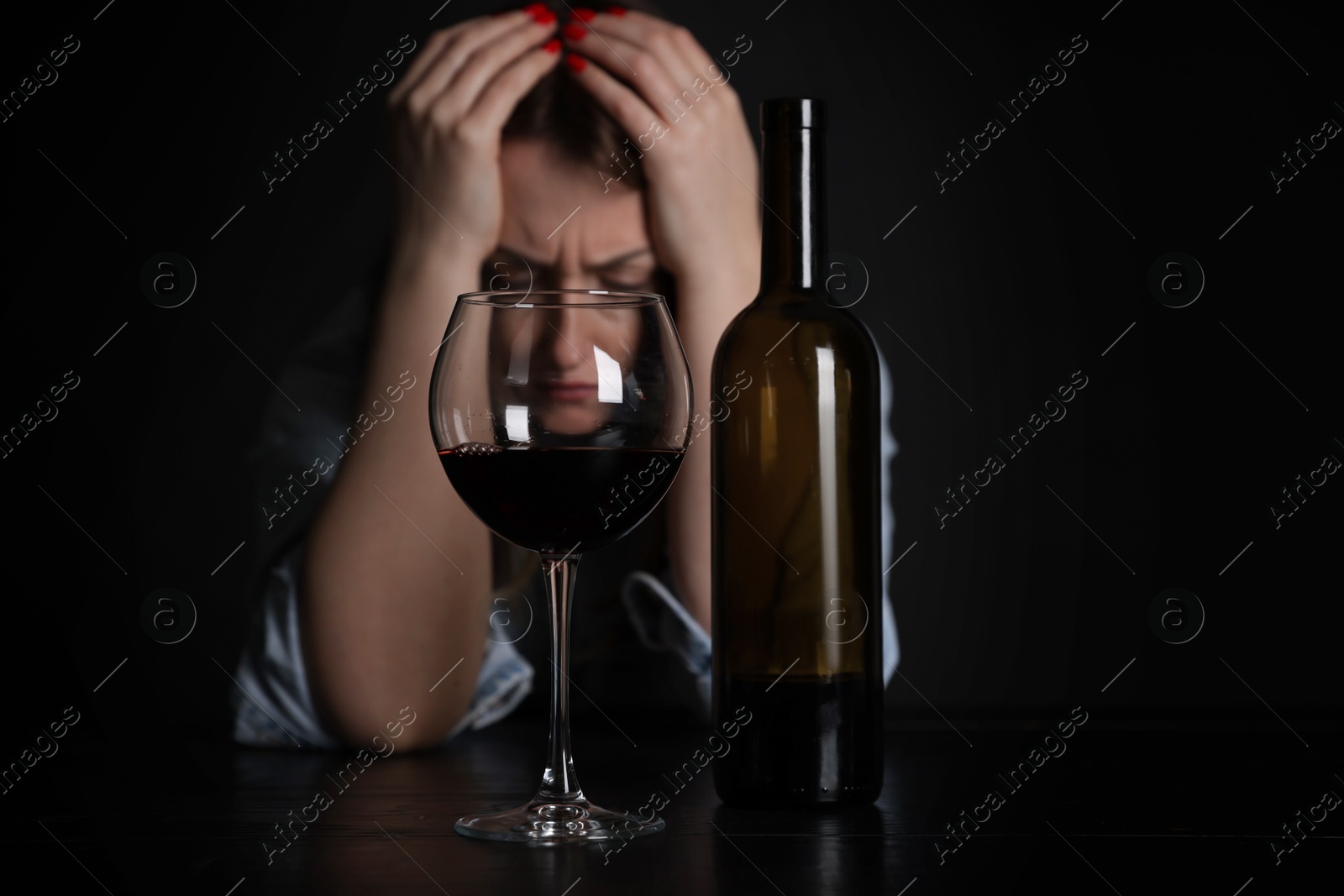 Photo of Alcohol addiction. Miserable woman with wine at table in dark