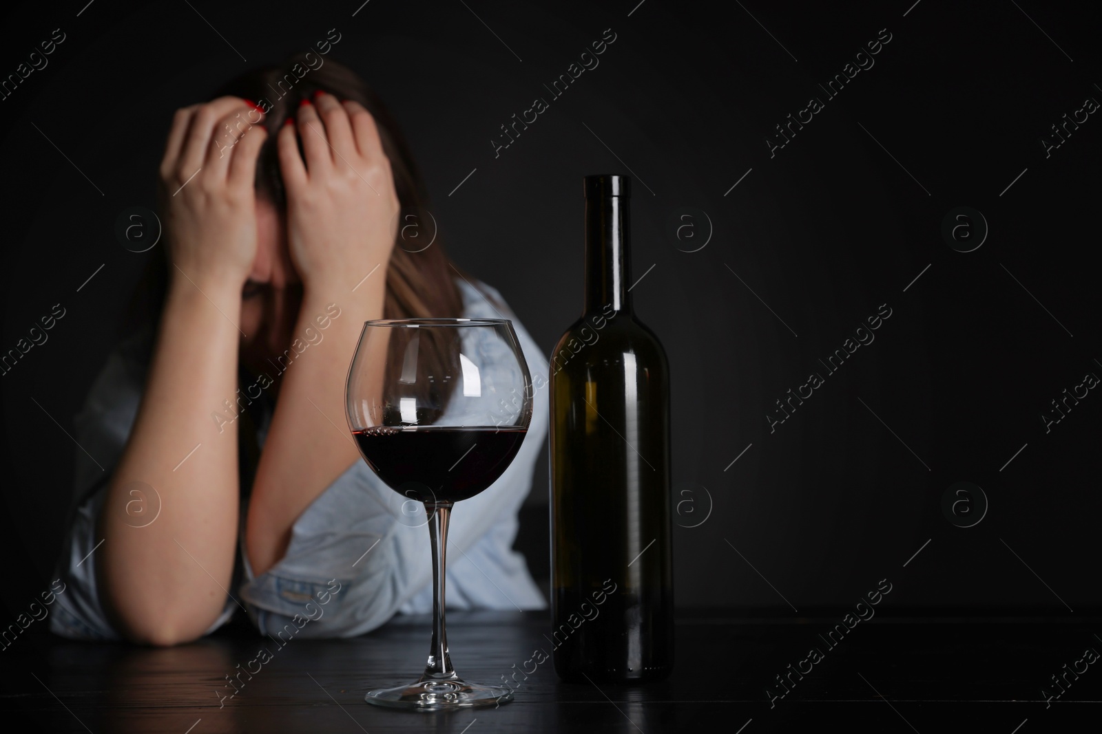 Photo of Alcohol addiction. Miserable woman with wine at table in dark. Space for text