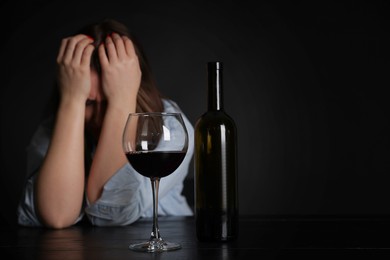 Photo of Alcohol addiction. Miserable woman with wine at table in dark. Space for text