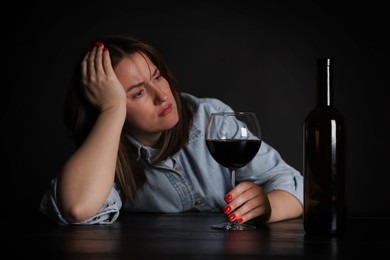 Photo of Alcohol addiction. Miserable woman with wine at table in dark