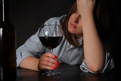 Photo of Alcohol addiction. Miserable woman with wine at table in dark