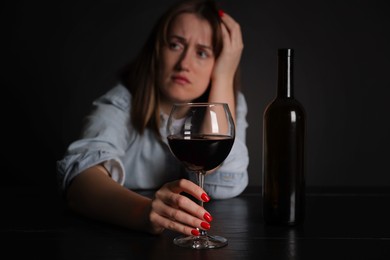 Photo of Alcohol addiction. Miserable woman with wine at table in dark, selective focus