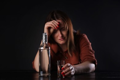 Photo of Alcohol addiction. Miserable woman with vodka at table in dark