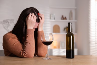 Photo of Alcohol addiction. Miserable woman with wine at table indoors