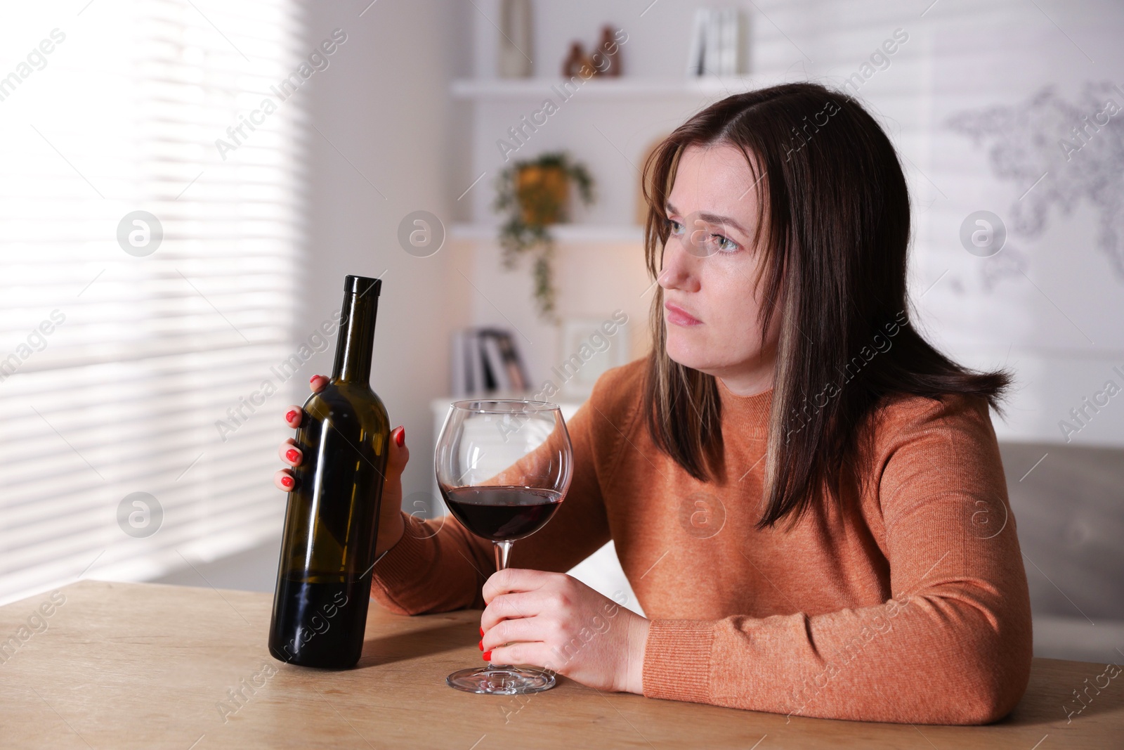 Photo of Alcohol addiction. Miserable woman with wine at table indoors