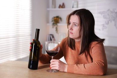 Photo of Alcohol addiction. Miserable woman with wine at table indoors