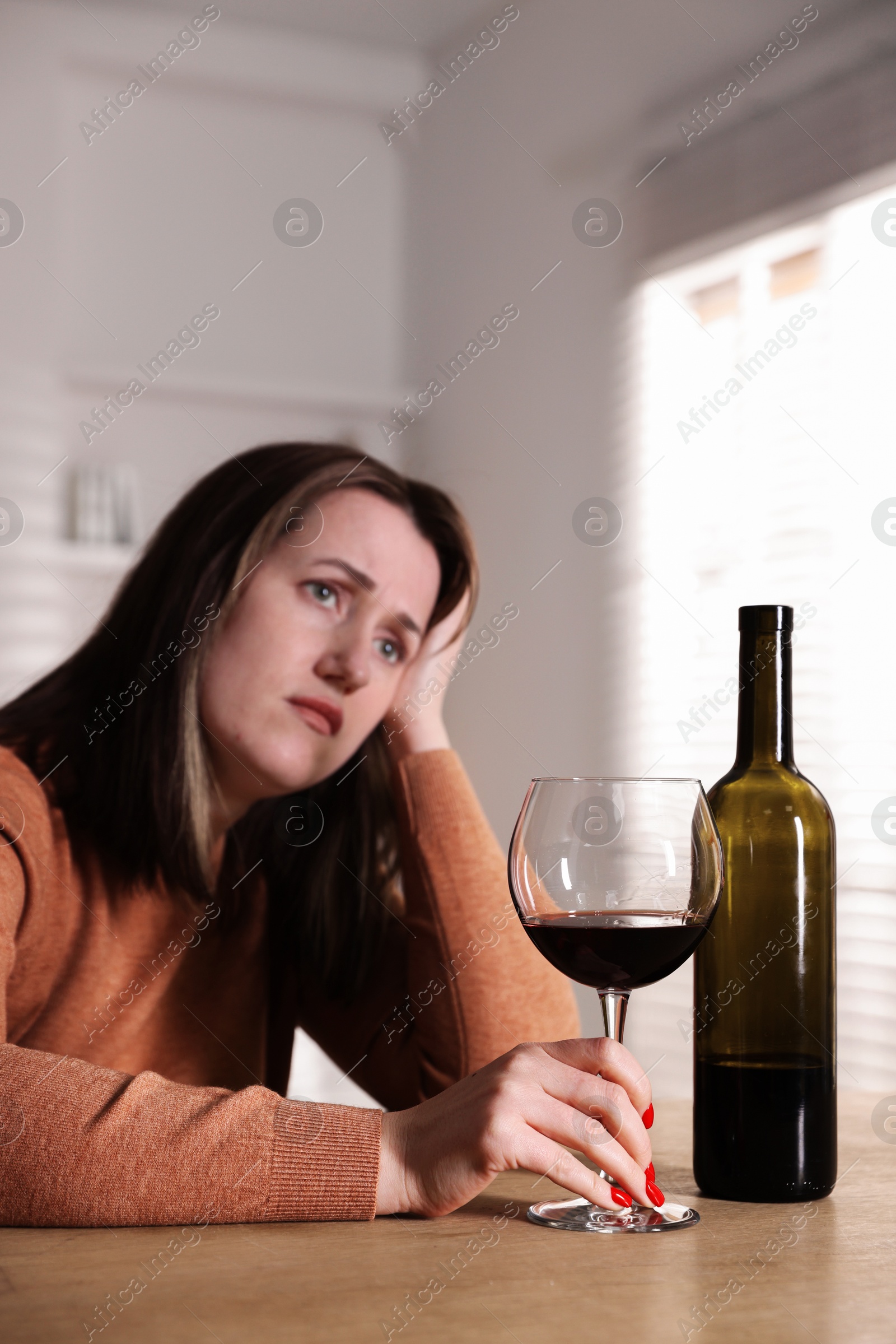 Photo of Alcohol addiction. Miserable woman with wine at table indoors, selective focus