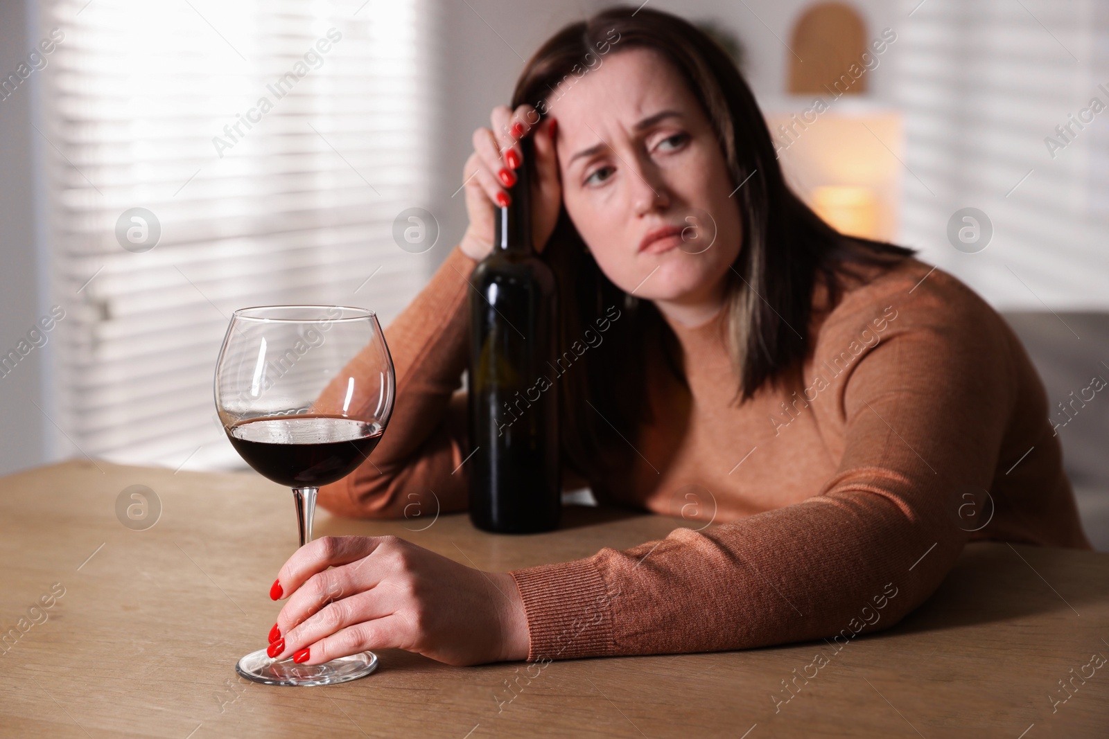 Photo of Alcohol addiction. Miserable woman with wine at table indoors, selective focus