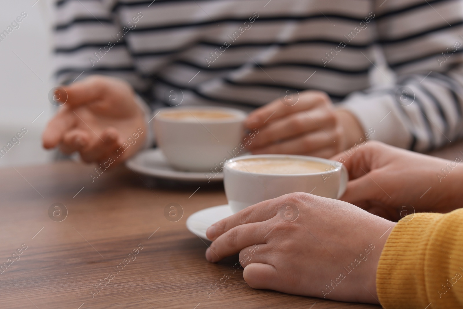 Photo of Coffee break. Women with cups of hot drinks at wooden table indoors, closeup