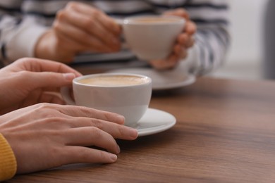 Photo of Coffee break. Women with cups of hot drinks at wooden table indoors, closeup