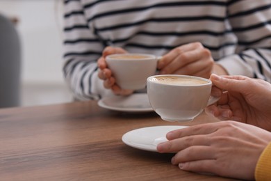 Photo of Coffee break. Women with cups of hot drinks at wooden table indoors, closeup