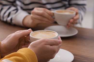 Photo of Coffee break. Women with cups of hot drinks at wooden table indoors, closeup