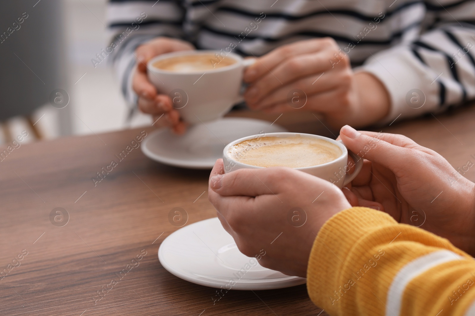 Photo of Coffee break. Women with cups of hot drinks at wooden table indoors, closeup