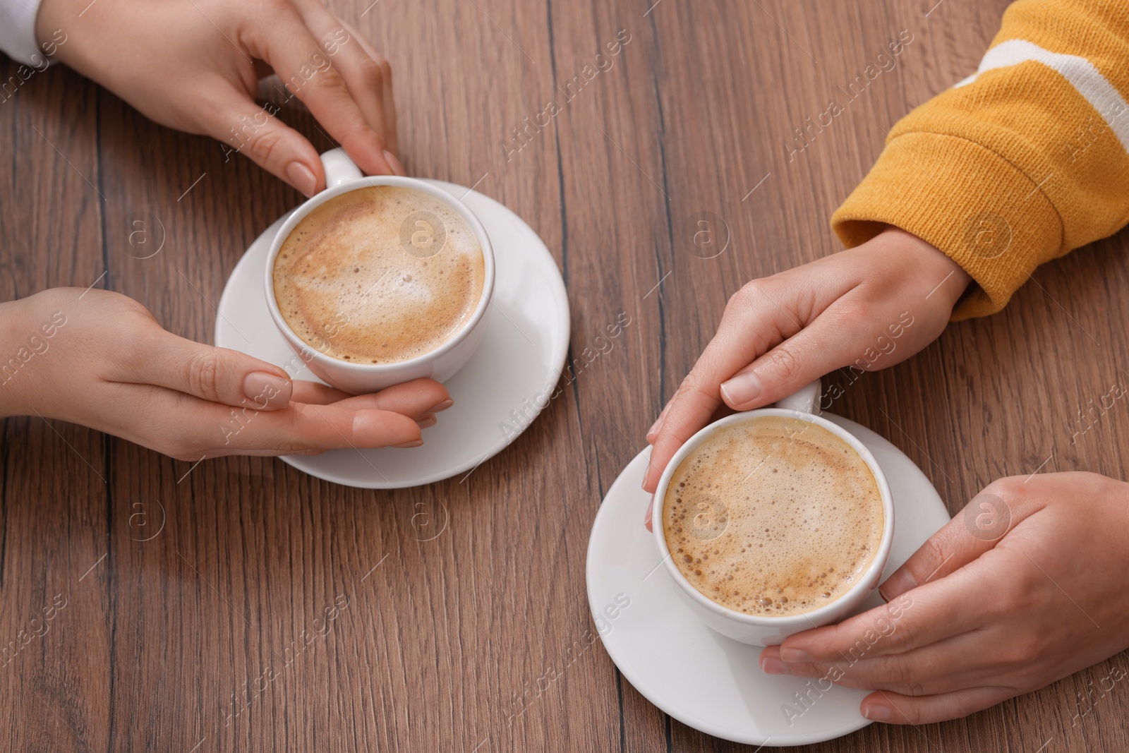 Photo of Coffee break. Women with cups of hot drinks at wooden table, closeup