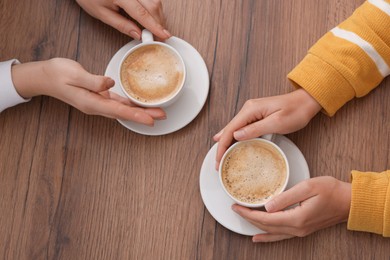 Photo of Coffee break. Women with cups of hot drinks at wooden table, top view