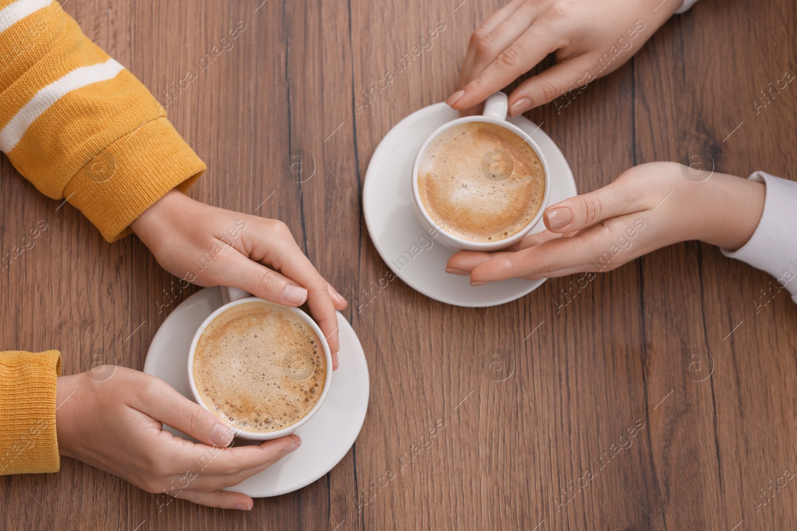 Photo of Coffee break. Women with cups of hot drinks at wooden table, top view