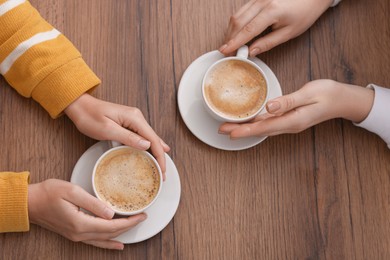 Photo of Coffee break. Women with cups of hot drinks at wooden table, top view