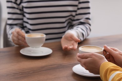 Photo of Coffee break. Women with cups of hot drinks at wooden table indoors, closeup