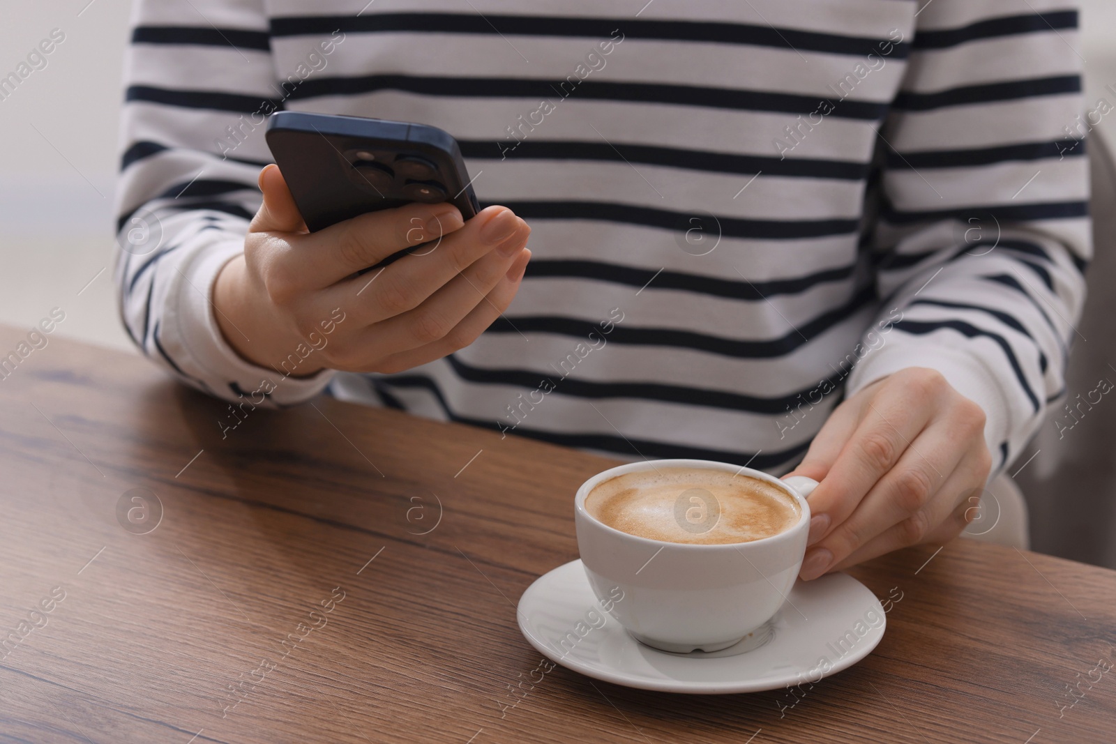 Photo of Woman using smartphone during coffee break at wooden table indoors, closeup