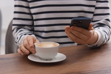 Photo of Woman using smartphone during coffee break at wooden table indoors, closeup